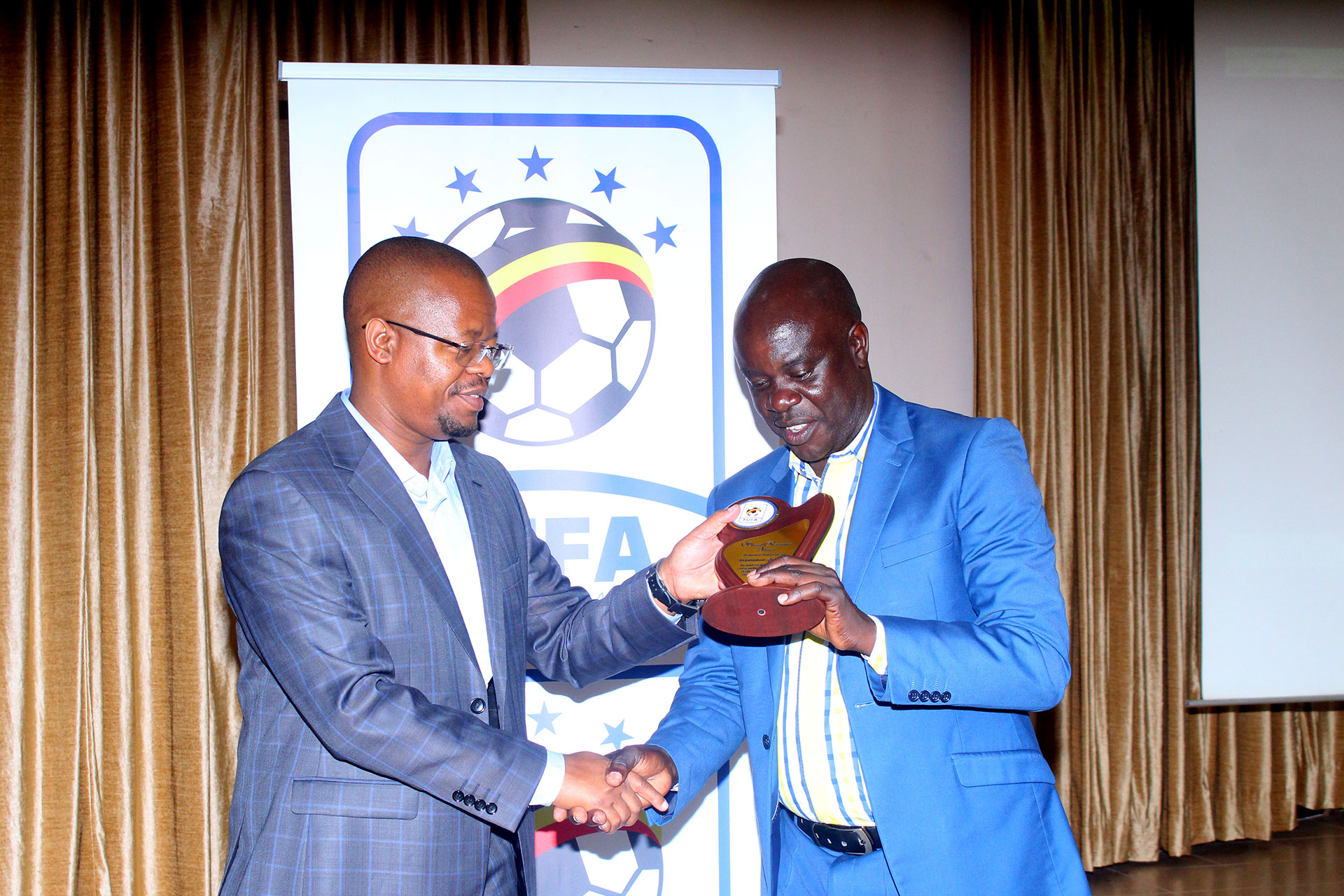 former FUFA communications Manager Rogers Mulindwa (R) receives appreciation accolade from FUFA President